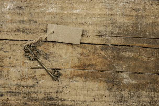 oude sleutel met label of tag over houten textuur achtergrond - Foto, afbeelding