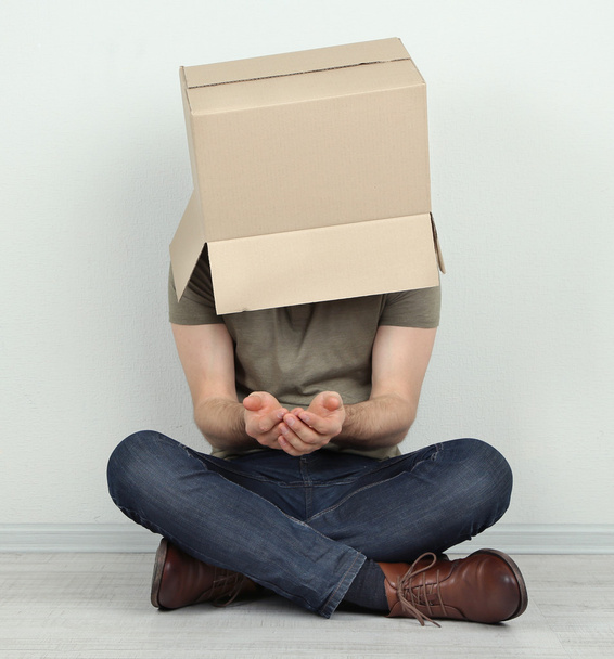 Man with cardboard box on his head sitting on floor near wall - Foto, immagini