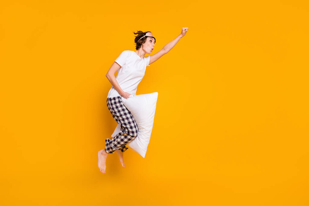 Full body photo of pretty funny lady pillow between legs jump fly ahead superhero playful mood energetic wear mask white t-shirt plaid pajama pants barefoot isolated yellow color background - Foto, afbeelding