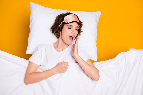 Photo of pretty peaceful lady satisfied enjoy morning covered warm blanket lying pillow eyes closed joyful facial expression wear mask white pajama t-shirt isolated yellow color background - Photo, Image