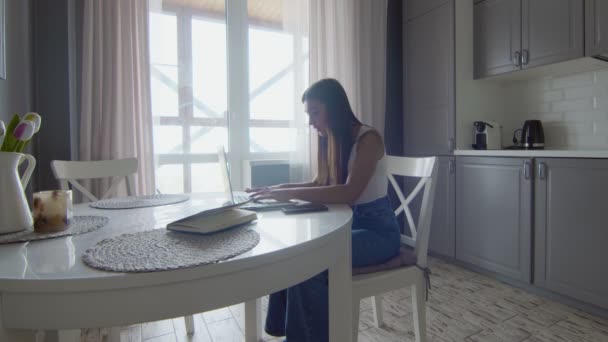 Jonge moderne vrouw praten op mobiel gebruik laptop in keuken interieur. - Video