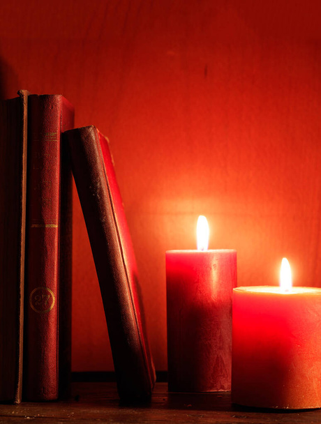 Vanhat kirjat ja valaistut kynttilät puupöydällä, kynttilänvalo punainen väri tausta, pystysuora - Valokuva, kuva