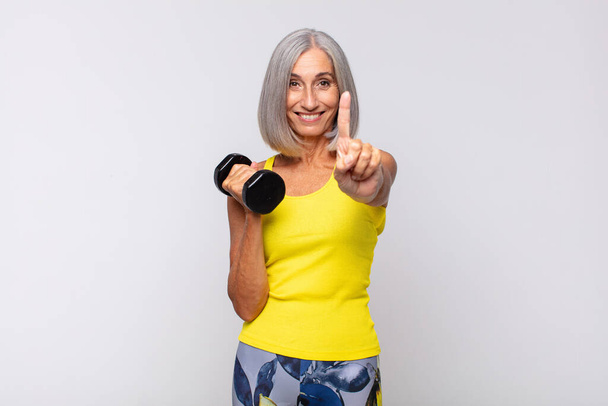 middle age woman smiling and looking friendly, showing number one or first with hand forward, counting down. fitness concept - Foto, Imagem