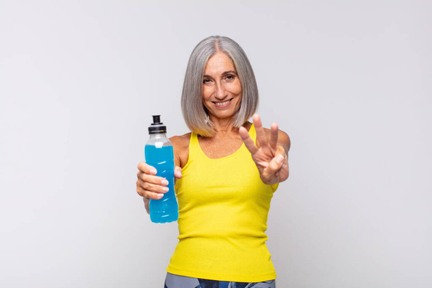 middle age woman smiling and looking friendly, showing number three or third with hand forward, counting down. fitness concept - Foto, Imagen