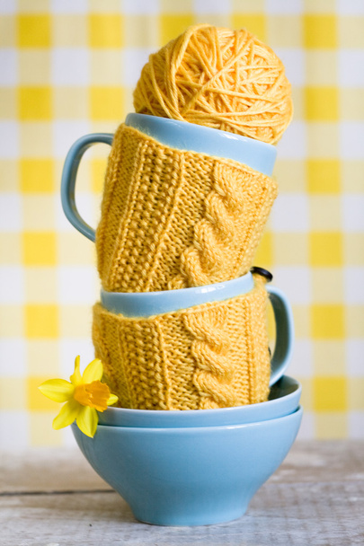 Dos tazas azules en suéter amarillo sobre una tela
 - Foto, Imagen