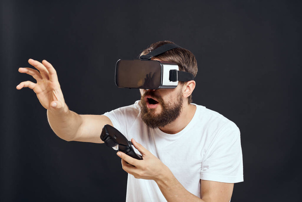 man het dragen van virtual reality bril met gamepad in de hand technologie games leisure donkere achtergrond - Foto, afbeelding