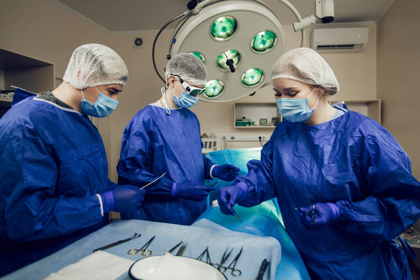 Porträt eines Chirurgenteams bei der Arbeit. Drei Ärzte mit medizinischen Masken bei Operationen beginnen mit der Operation des Patienten - Foto, Bild