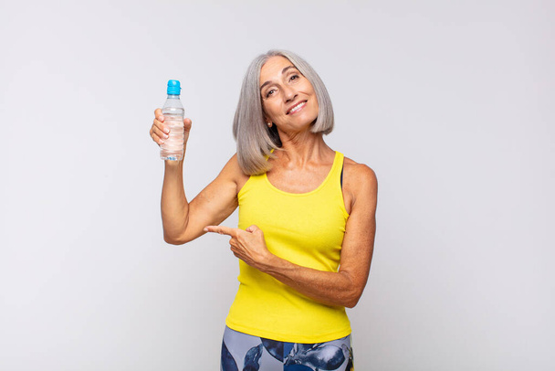 middle age woman smiling cheerfully, feeling happy and pointing to the side and upwards, showing object in copy space. fitness concept - Foto, afbeelding