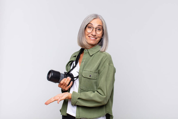 middle age woman smiling cheerfully, feeling happy and showing a concept in copy space with palm of hand. photographer concept - Foto, imagen