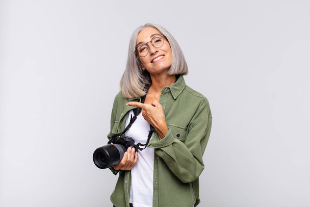 middle age woman smiling cheerfully, feeling happy and pointing to the side and upwards, showing object in copy space. photographer concept - Фото, изображение