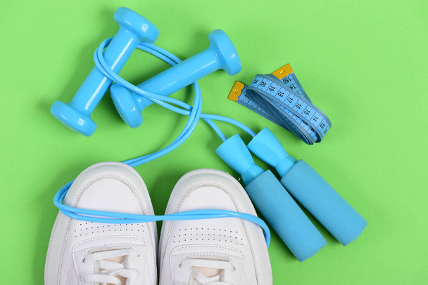 Sneakers with skipping rope and tape on green background. - Фото, зображення