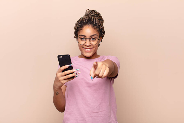 young afro woman pointing at camera with a satisfied, confident, friendly smile, choosing you. smart phone concept - Φωτογραφία, εικόνα