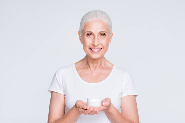 Portrait of charming retiree in stylish trendy t-shirt holding jar with lotion isolated over white t-shirt isolated over white background - Фото, изображение
