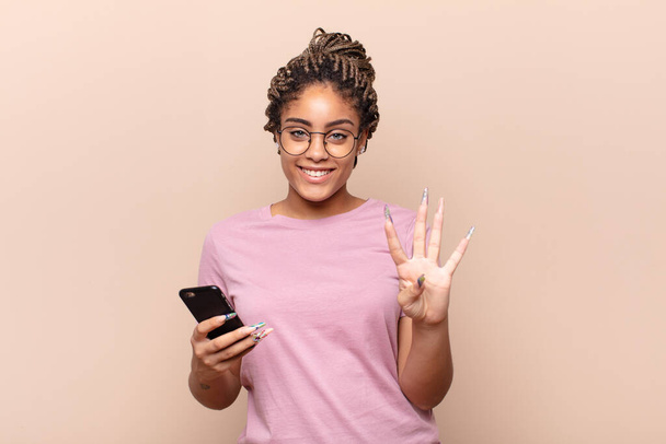 young afro woman smiling and looking friendly, showing number four or fourth with hand forward, counting down. smart phone concept - Φωτογραφία, εικόνα