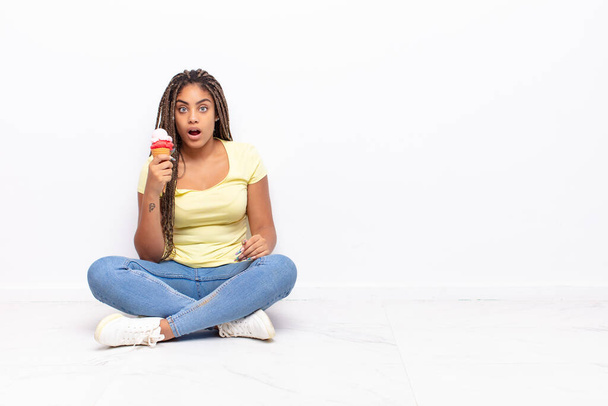 young afro woman looking very shocked or surprised, staring with open mouth saying wow. ice cream concept - Photo, image