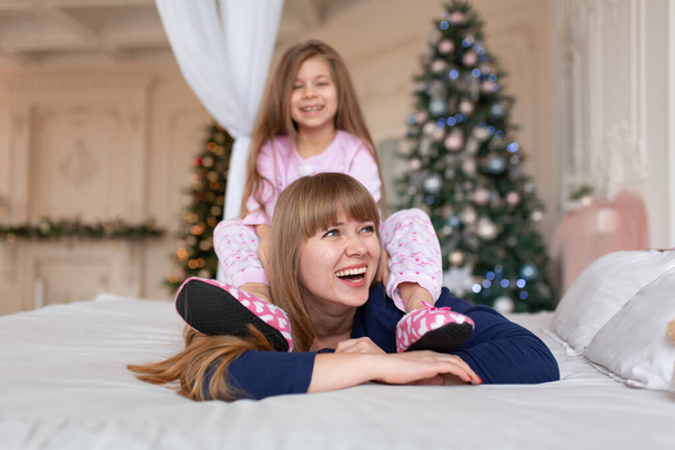 Little girl spends time playing with mom while lying in bed. Christmas tale. Happy childhood. - Valokuva, kuva
