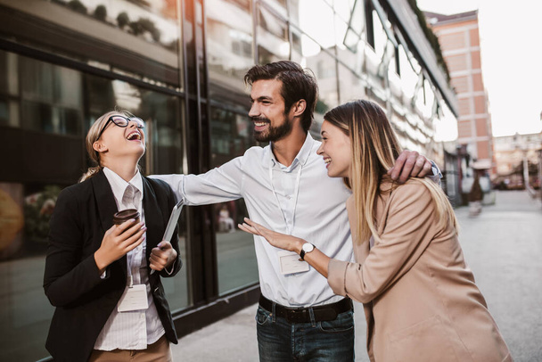 Three cheerful young business people talking to each other while walking outdoors - Фото, изображение