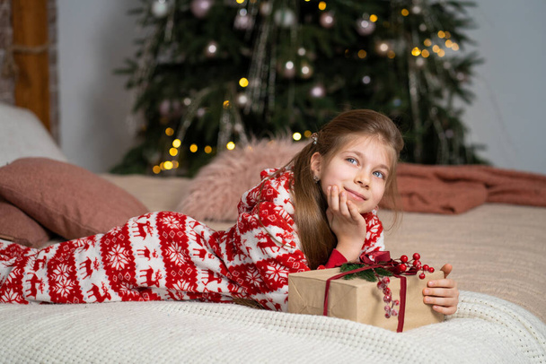 A little girl in pajamas early in the morning found a present from Santa under the tree. Christmas magic fairy tale. Happy childhood. - Φωτογραφία, εικόνα