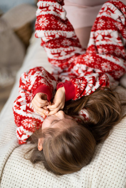 Pieni tyttö punaisessa pyjamassa leikkii äidin kanssa sängyssä. - Valokuva, kuva