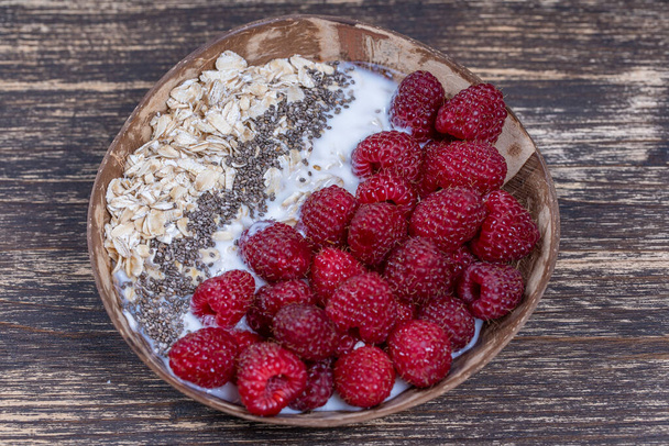 Smoothie in coconut bowl with raspberries, oatmeal and chia seeds for breakfast , close up. The concept of healthy eating, superfood. Top view - Фото, изображение