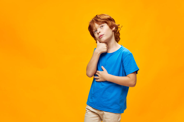 Rudowłosy chłopiec zamyślony twarzy ekspresja trzymać rękę w pobliżu głowy marzycielski wygląd niebieski t-shirt  - Zdjęcie, obraz