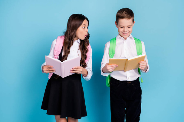 Photo of two little girl boy schoolchildren brother sister classmates hold textbook unexpected unbelievable high grade wear bag white shirt black pants dress isolated blue color background - 写真・画像