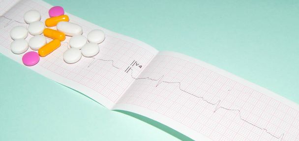 Medications in the form of tablets for oral administration against the background of an electrocardiogram. The heartbeat is shown on the graph, blue background - Fotó, kép