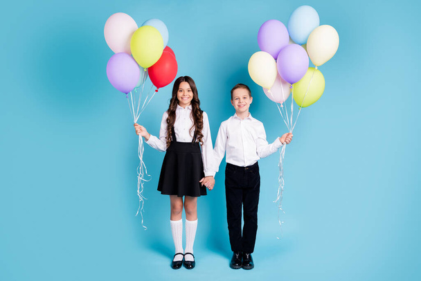 Full length photo of two little girl boy schoolchildren best friends sister brother hold hands balloons 1-september white shirt black pants dress shoes isolated blue color background - Photo, Image