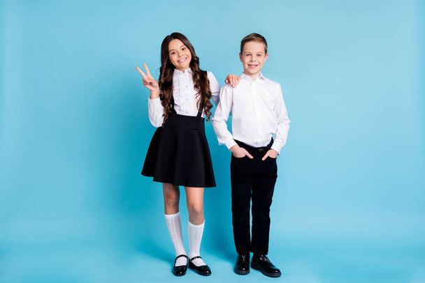Hello schoolkid. Full length photo of two girl boy model schoolchildren classmates sister brother show v-sign wear uniform white shirt black pants dress shoes isolated blue color background - Foto, immagini