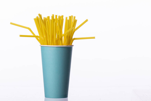 Yellow plastic flexible straws in blue paper cup isolated on white background - Photo, Image