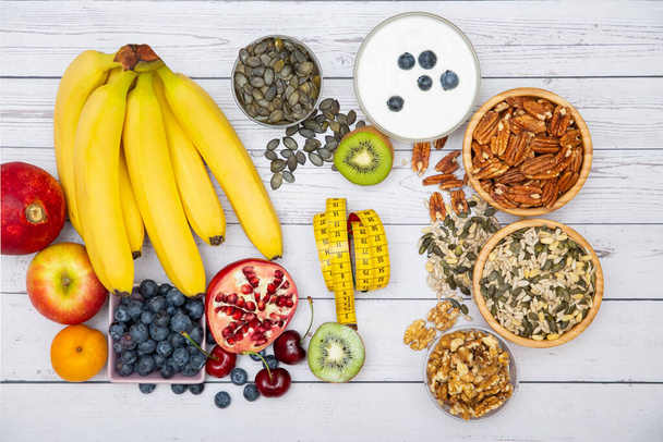 Ομάδα Ξηροί καρποί που τοποθετούνται στο μπολ και φρούτα είναι μπανάνα, ανανάς και σταφύλι είναι τα τρόφιμα υγιεινά στο ξύλινο τραπέζι φόντο - Φωτογραφία, εικόνα