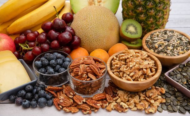 Групові горіхи на мисці та фрукти це банан, ананас та виноград це їжа, здорова на дерев'яному столі
 - Фото, зображення