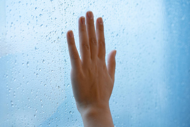 Female hand at the window during the rain. Glass in drops of water - Photo, Image