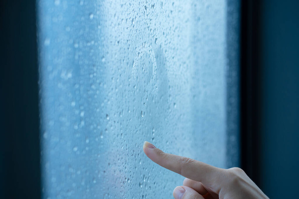 Female hand draws a question mark on a foggy window during the rain. A glass in drops of water - 写真・画像