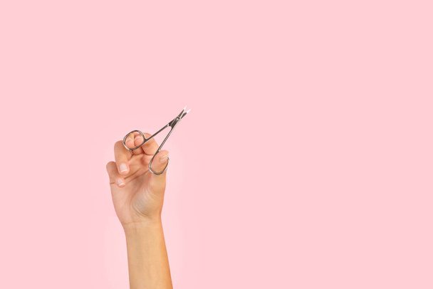 Woman hand holding a manicure scissors on a pink background with copy space - Fotoğraf, Görsel