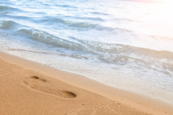Close-up van de strandkust met een mannenvoetafdruk op het gele zand langs de lijn van de blauwe zeegolf op een zomerzonnige dag. Achtergrond voor advertentiereizen of toeristische vakanties. - Foto, afbeelding