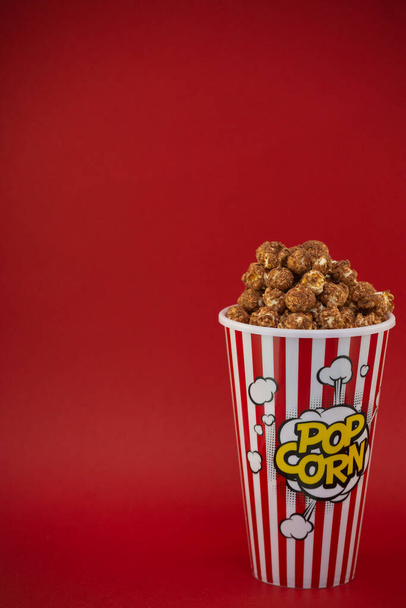 Du pop-corn au beurre dans une tasse de pop-corn rouge, une collation à la maison ou au cinéma sur fond rouge - Photo, image