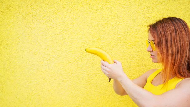 Red-haired woman holding a banana depicting a pistol shot - Photo, image
