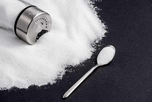 Белая морская соль для приготовления пищи в маленькой стеклянной бутылке. На солевом фоне пишите стоп. Концепция здоровья - Фото, изображение