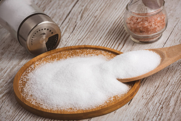 Bílá mořská sůl pro vaření potravin v malých skleněných lahvích, dřevěné lžíce, a podnosy na starém dřevěném stole Pozadí. - Fotografie, Obrázek