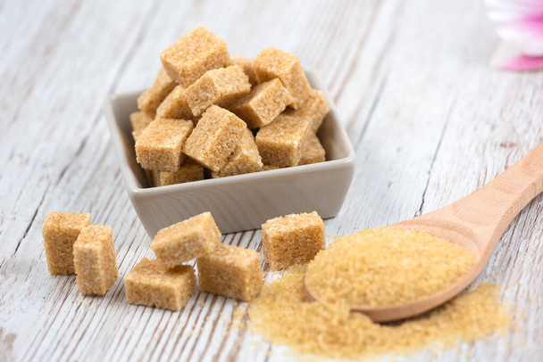 Bruine suiker in een vierkante kop en houten lepel op een houten tafel, gezonde suiker wordt gebruikt voor het koken van voedsel of desserts. - Foto, afbeelding