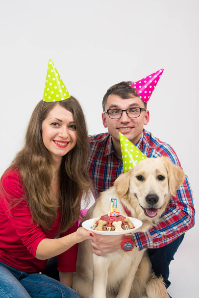 Junge Familie mit ihrem Hund Golden Retriever feiert einen einjährigen Geburtstag. Freundschaft. Liebe. Familie. Studioporträt auf weißem Hintergrund - Foto, Bild