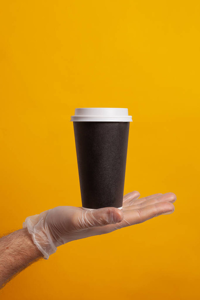 A hand in a glove holds a disposable cup - 写真・画像