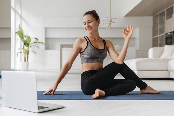 Instrutora de ioga feminina mostrando exercício durante a realização de aula on-line por videoconferência. Mulher desportiva praticando ioga em sua sala de estar usando laptop para aula virtual. Estilo de vida saudável, bem-estar - Foto, Imagem