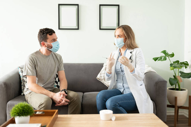 Γιατρός και ασθενής φορώντας μάσκες προσώπου ενώ ο γιατρός μιλά για πιθανή δευτερογενή επίδραση ενός εμβολίου που πρόκειται να εφαρμόσει - Φωτογραφία, εικόνα