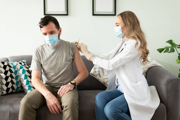 Portrait of a man in his 30s wearing a face mask and getting ready to be vaccinated from a female doctor - Photo, Image