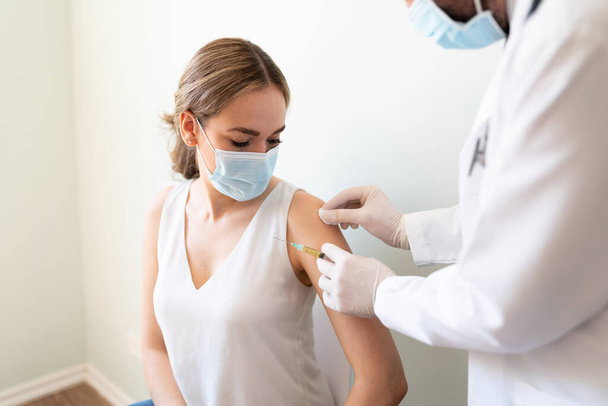 Médico usando um cotonete com álcool para limpar o braço de uma mulher antes de aplicar uma vacina no consultório médico - Foto, Imagem