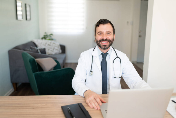Porträt eines gut aussehenden hispanischen Arztes, der von zu Hause aus mit Patienten spricht und lächelt - Foto, Bild