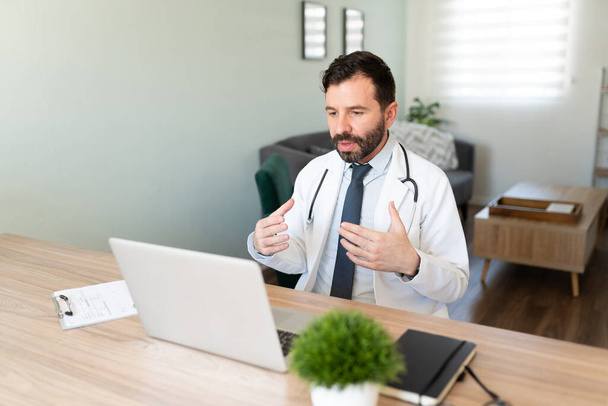 Portret wirtualnego hiszpańskiego lekarza udzielającego porad medycznych pacjentowi podczas rozmowy wideo podczas pracy w domu - Zdjęcie, obraz
