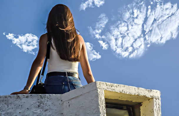 Teenager with white T-shirt and jeans skirt on top of a wall in the evening - Photo, Image